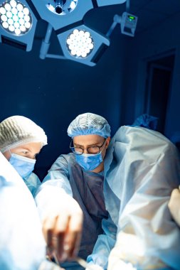 Cerrahlar ameliyathanede. Tıp uzmanları steril bir ameliyathanede parlak ışıkları olan bir cerrahi müdahaleye odaklandılar..