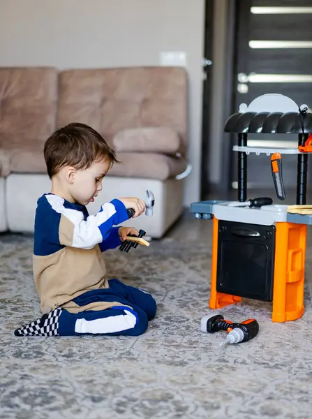 İçeride aletleri olan çocuk oyuncakları. Küçük bir çocuk oturma odasındaki halıya oturur, oyuncak aletlerle yaratıcı bir oyun oynar gibi mutfağa geçer..