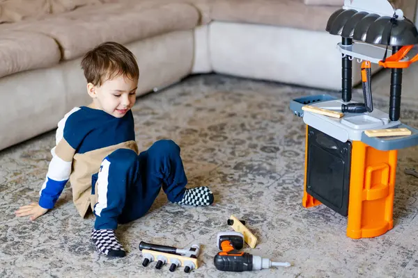 Çocuk oyuncak aletlerle oynuyor. Çocuk, oyuncak tezgahıyla yaratıcı oyunlardan ve rahat bir oturma odasında rahat bir halıda aletlerden hoşlanıyor..