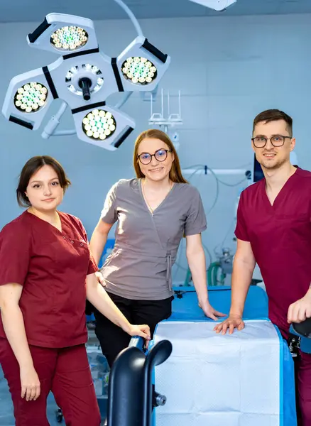 Cerrahi sağlık uzmanları. Üç sağlık uzmanı, gündüz vakti parlak bir cerrahi ameliyathanede güven içinde poz veriyorlar..