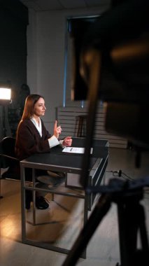 Bir blogun stüdyo görüntüleri. Masada oturan esmer kadın kameraya konuşuyor. Blog yazarının etrafında dolaşır. Dikey video.