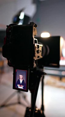Tripodda çalışan profesyonel kamera. Modern fotoğraf stüdyosunda bir kadın blogcuyu kaydediyor. Dikey video.