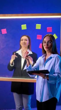Pozitif proaktif kadınlar ofiste beyin fırtınası yapıyor. Kadınlar fikirleri planlamak ve yönetmek için yapıştırmalı cam tahta kullanırlar. Dikey video.