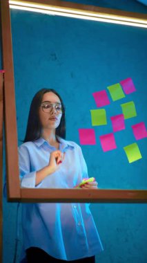 Kendine güvenen, genç, beyaz bir kadın cam levhadan çıkartmalar çıkarıyor. Fikir kavramı, iş stratejisi. Dikey video.