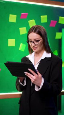 Beyaz iş kadını tabletine bakıyor. Kameraya bakarak kendine güvenen mutlu bir kadının portresi. Dikey video.