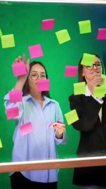 Ofis çalışanları cam tahtaya etiket yapıştırıyor. Beyin fırtınası ya da iş sunumu için hazırlık. Dikey video.