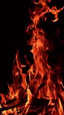 Büyük bir kamp ateşinde yanan kuru tahta çubuklar. Gece yerde büyük şenlik ateşi yanıyor. Dikey video
