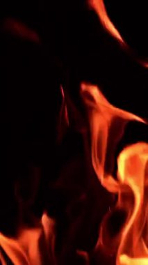 Zifiri karanlıkta dans eden alevler. Alevlerin dilleri ileri geri sallanıyor ve gece parıldıyor. Dikey video