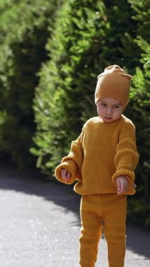Sarı örgü takım elbiseli sevimli çocuk dışarıda duruyor. Küçük çocuk ilgi çekici bir şeye bakıyor. Dikey video