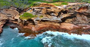 Bazı yerlerdeki kaya oluşumları suyla kırılmış. Dalgalar kıyıya vurur kayalara.