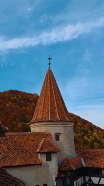 Romanya 'nın Transilvanya kentindeki Bran kalesinin çatıları. Renkli sonbahar doğası ve mavi gökyüzü arka planda. Dikey video