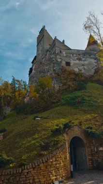Yüksek tepede duran kalenin gizli girişi. Renkli sonbahar sezonunda Bran Kalesi 'nin alçak açılı görüntüsü. Dikey video