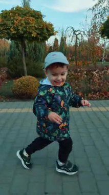 Enerjik neşeli çocuk sonbaharda parkın etrafında koşar. Dışarıda iyi vakit geçirmenizi dilerim. Dikey video