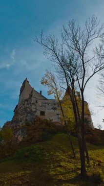 Üstünde Bran Castle olan yeşil tepe. Güzel bir ortaçağ şatosu ve güzel bir sonbahar şatosu. Düşük açı. Dikey video
