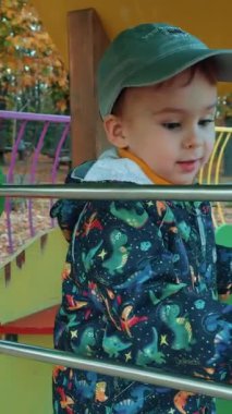 Güzel beyaz çocuk oyun bahçesinde abaküsle oynuyor. Erkek çocuk sonbaharda dışarıda iyi vakit geçiriyor. Dikey video