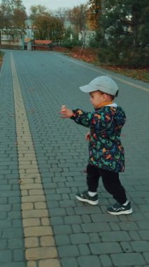 Tatlı beyaz çocuk sonbahar parkının yanından geçiyor. Küçük çocuk ellerin büyük heykelini fark eder ve onlara dokunmaya gelir. Dikey video