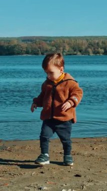 Kafkasyalı erkek çocuk suya taş atıyor. Bebeğim sonbaharda güneşli bir günde nehir kıyısında oynuyor. Dikey video