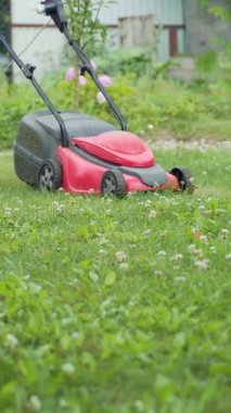 Adam yazın bahçede çim biçme makinesiyle çalışıyor. Çim biçme makinesi dikey video üzerinde çim biçiyor