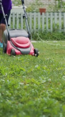 Bahçede çim biçme makinesiyle koşan bir çocuk. Bahçede çim biçiyorum. Dikey videoyu kapat
