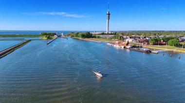 Hollanda, Lelystad 'daki Markermeer Gölü' nün su manzarasından motorlu tekneye yaklaşıyoruz. İnsansız hava aracı görüntüleri telekom kulesi ve yeşil şehir manzarasını gösteriyor..