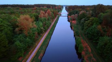 Üzerinde bir köprü olan ayna kanalının üzerinden uçuyor. Kanalın etrafında derin ormanlar yetişiyor. Gün batımı görüntüleri.