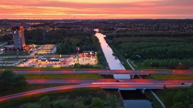 Karayollarının, otoparkların ve binaların alacakaranlıkta güzel aydınlanması. Şehrin ışıkları arka planda. Manzaranın üzerinde turuncu gökyüzü. Hava perspektifi.