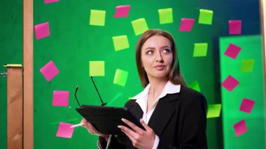 Siyah ceket giyen güzel esmer kadın cam tahtada duruyor. Düşünceli girişimci gözlük takar ve tabletine bakar..