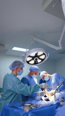 Bir grup erkek doktor ameliyatta çalışıyor. Erkek ameliyathane hemşiresi ameliyat masasından aletleri alıp doktora veriyor. Dikey video.