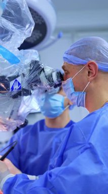 Mikroskoba bakan beyaz erkek doktorun gergin suratı. Cerrah elektrikli alet kullanarak ameliyat yapar. Dikey video.