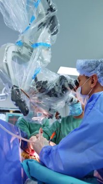 Profesyonel erkek cerrah nöroşirürjide elektrikli aletler kullanır. Doktor mikroskoba dikkatlice bakıyor. Düşük açı. Dikey video.