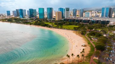 Yeşil park ile çevrili güzel kumlu sahil. Waikiki 'nin modern yüksek binaları arka planda. Hawaii, ABD.