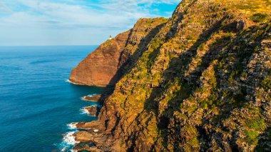 Sersemletici, ulaşılamaz kayalar okyanusa iniyor. Küçük deniz feneri uçurumun kenarında. Hawaii, ABD.