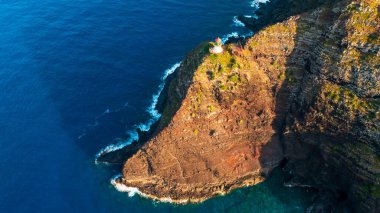 Sersemletici, ulaşılamaz kayalar okyanusa iniyor. Küçük deniz feneri uçurumun kenarında. Hawaii, ABD.