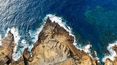 Köpüklü dalgalar kayalık kıyıya vuruyor. Kayalara çarpan suyun hipnotize edici güzel görüntüsü. Üst görünüm.