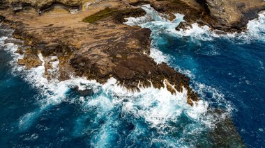 Su sıçratan okyanus dalgalarının oluşturduğu çıplak kayalar. Kıyı üzerinde deniz suyu fışkıran hava perspektifi. Hava görünümü.