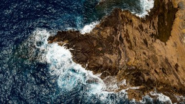 Su sıçratan okyanus dalgalarının oluşturduğu çıplak kayalar. Kıyı üzerinde deniz suyu fışkıran hava perspektifi. Hava görünümü.