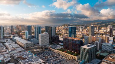 Yüksek binaların cephelerinde güneşin batışının parlak ışığı. Gün batımında Waikiki, Honolulu, Hawaii, ABD üzerindeki İHA uçuşu.