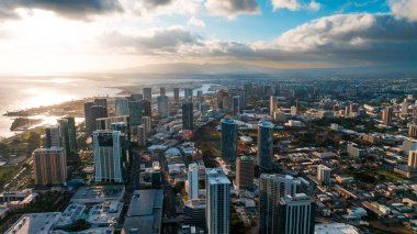 Yüksek binaların cephelerinde güneşin batışının parlak ışığı. Gün batımında Waikiki, Honolulu, Hawaii, ABD üzerindeki İHA uçuşu.