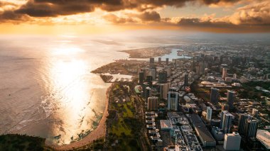 Pasifik Okyanusu dalgaları Waikiki, Honolulu, Hawaii, ABD kıyılarına ulaşır. Batan güneş manzarayı aydınlatıyor. Dağların üstündeki gökyüzünde turuncu bulutlar.