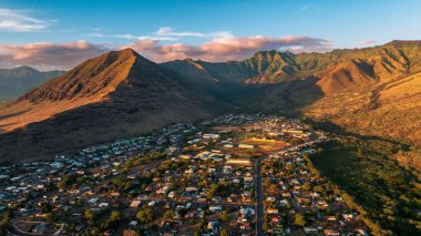 Çıplak dağlarla çevrili düşük katlı bir şehir manzarası. Kayaların üzerinde bulutlu bir hava var. Honolulu, Hawaii, ABD. Hava görünümü.