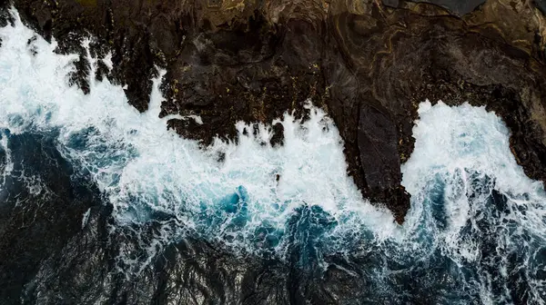 Su sıçratan okyanus dalgalarının oluşturduğu çıplak kayalar. Kıyı üzerinde deniz suyu fışkıran hava perspektifi. Hava görünümü.