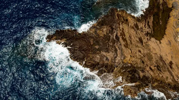 Su sıçratan okyanus dalgalarının oluşturduğu çıplak kayalar. Kıyı üzerinde deniz suyu fışkıran hava perspektifi. Hava görünümü.
