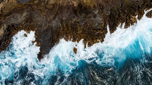 Su sıçratan okyanus dalgalarının oluşturduğu çıplak kayalar. Kıyı üzerinde deniz suyu fışkıran hava perspektifi. Hava görünümü.