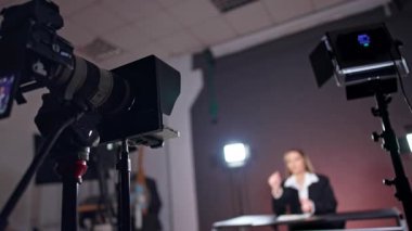Stüdyoda profesyonel fotoğraf ekipmanları var. Düşük açı. Bulanık arkaplanda konuşan bir kadının görüntüsü.