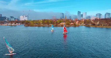 Renkli yelkenli yelkenliler nehir kıyılarında hareket ediyor. Boston limanına yaklaşan Charles Nehri üzerindeki drone görüntüleri sis ile kaplı..