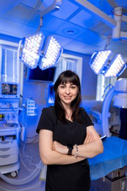 Modern ameliyathanede cerrah. Kendine güvenen bir cerrah, iyi donanımlı bir ameliyathanede kollarını kavuşturup mavi ışıklarla aydınlatır..