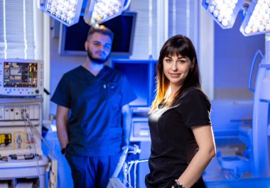 Ya da sağlık uzmanları. Modern ve iyi aydınlatılmış bir ameliyathanede gelişmiş tıbbi ekipmanlarla birlikte iki sağlık uzmanı duruyor..