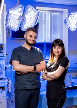 Modern bir ameliyathanede doktorlar. İki sağlık hizmeti sağlayıcısı gelişmiş cerrahi ışıklarla donatılmış son teknoloji ürünü bir ameliyathanede güven içinde poz veriyorlar..