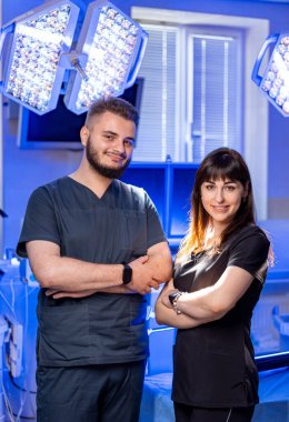 Doktorlar ameliyathanede poz verirler. Önlüklü iki sağlık uzmanı parlak bir ameliyathanede hazır bekliyor..