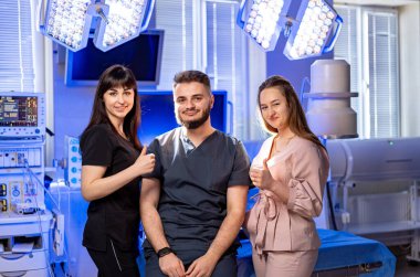 Sağlık uzmanları başarıyı kutluyor. Üç sağlık uzmanı modern bir tıbbi tesiste gururla poz veriyor, takım çalışması ve başarı sergiliyorlar..